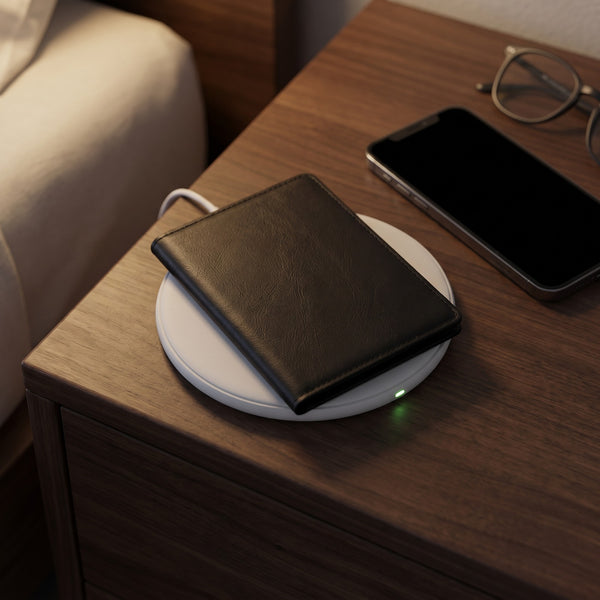 The passport cover charging on a wireless charging pad on a nightstand